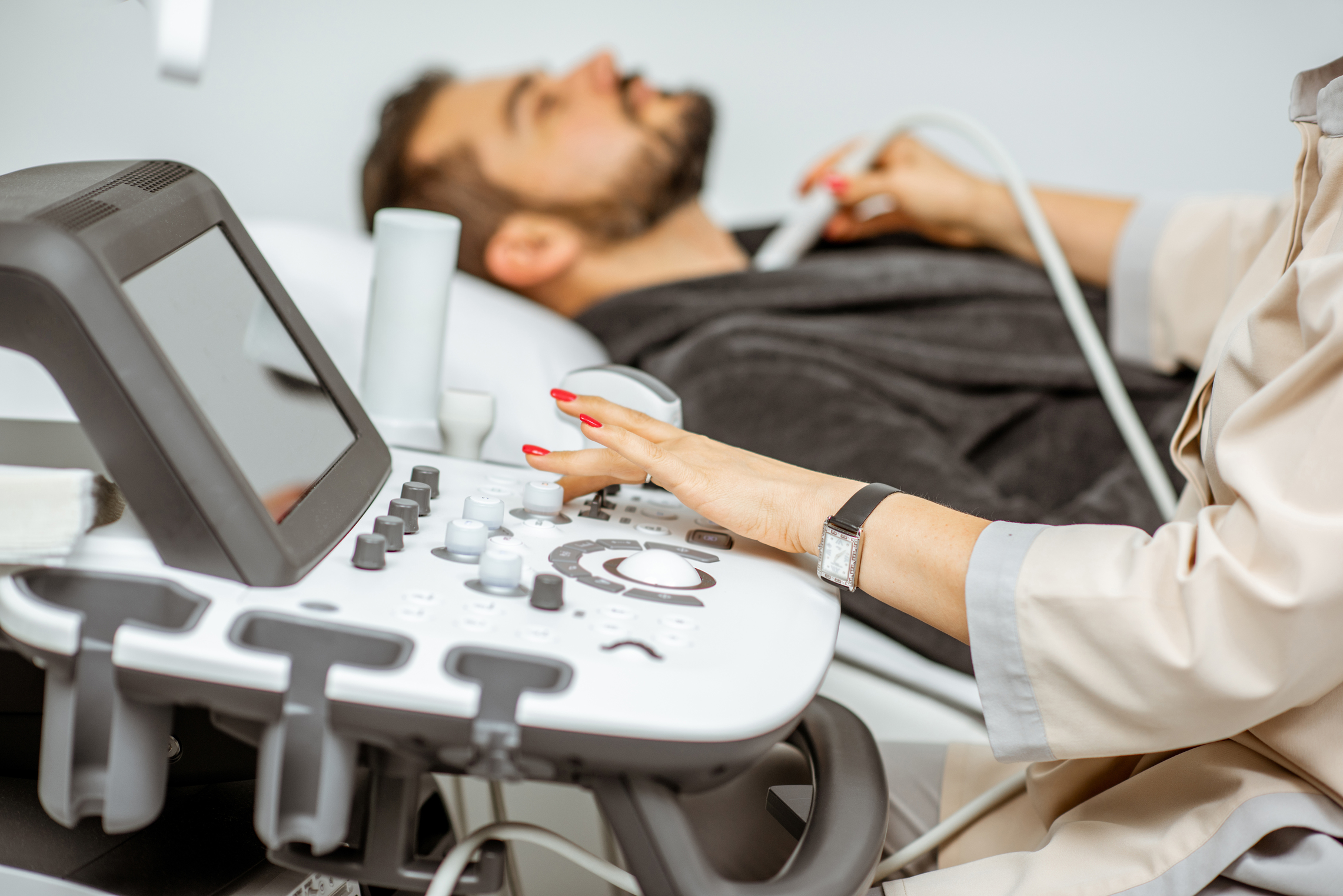 Men examining his thyroid with ultrasound sensor, lying in bathrobe on the couch at the medical office