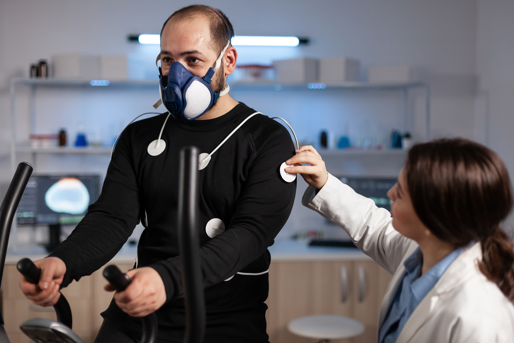 Specialist woman researcher putting electrodes sensor on sportman with mask monitoring EGK data in medical mordern laboratory. Athlete man running on fintess trainer working at body endurance